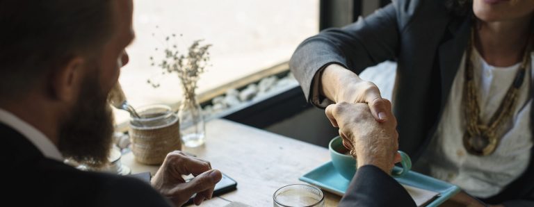 Man and a woman shaking hands while sitting at a restaurant