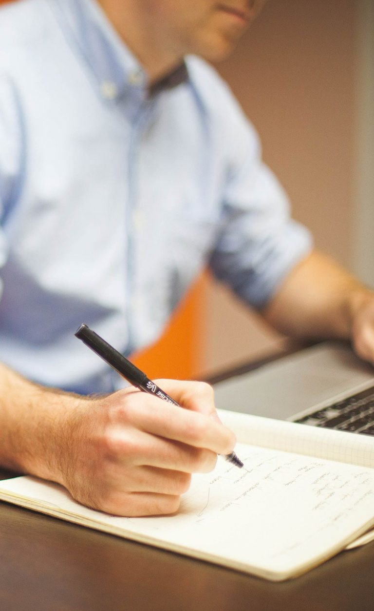 Man writing by a laptop in an office